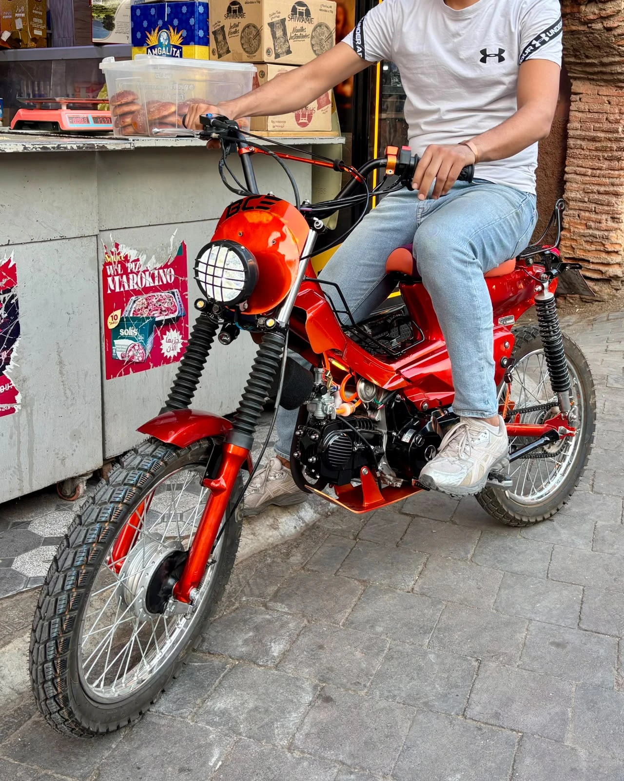 Cadi Ayyad custom red motorcycle with rider near a Marrakech street shop