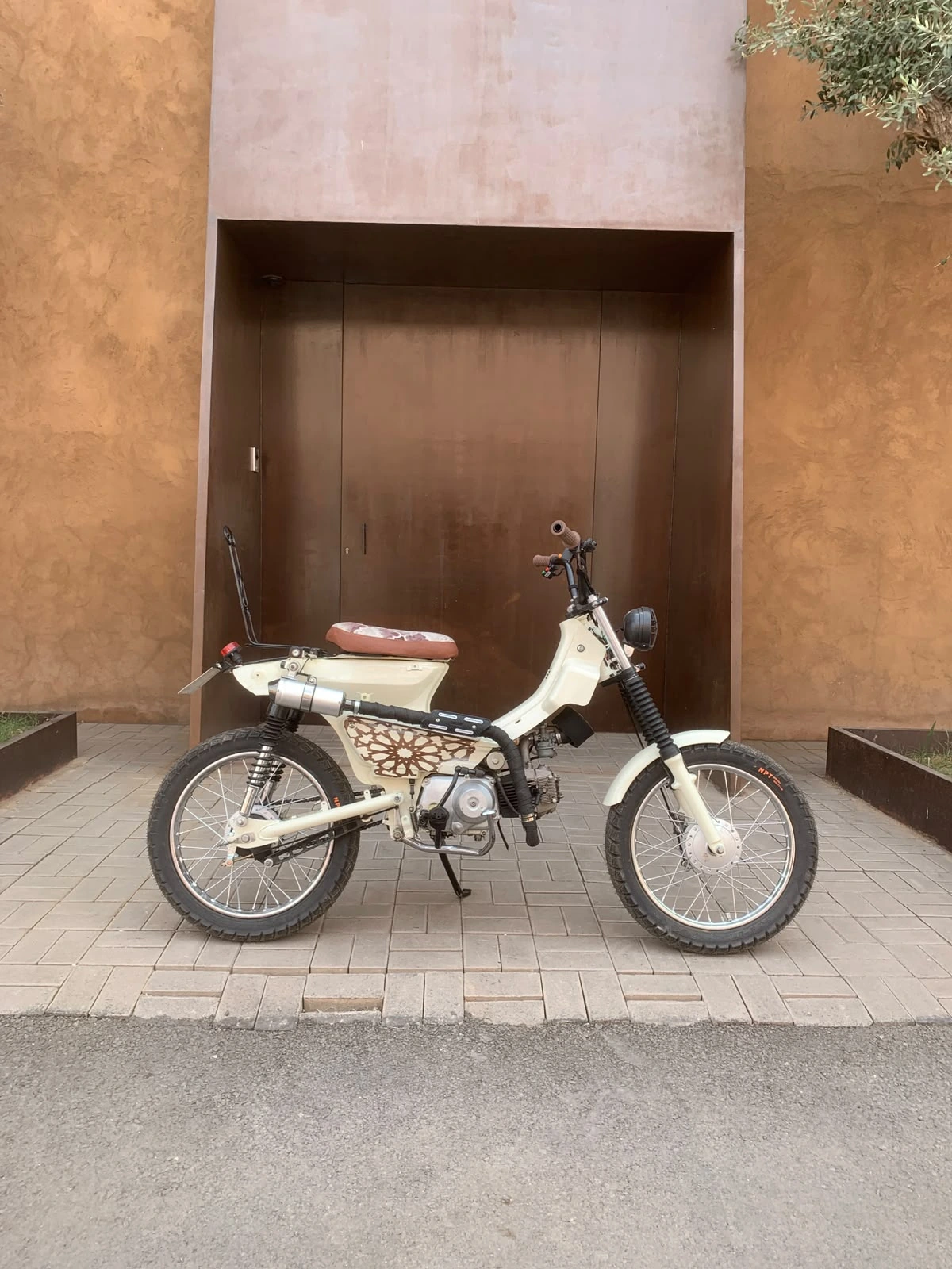 Mouad El Baraka custom motorcycle side profile in front of Moroccan earth-tone architecture