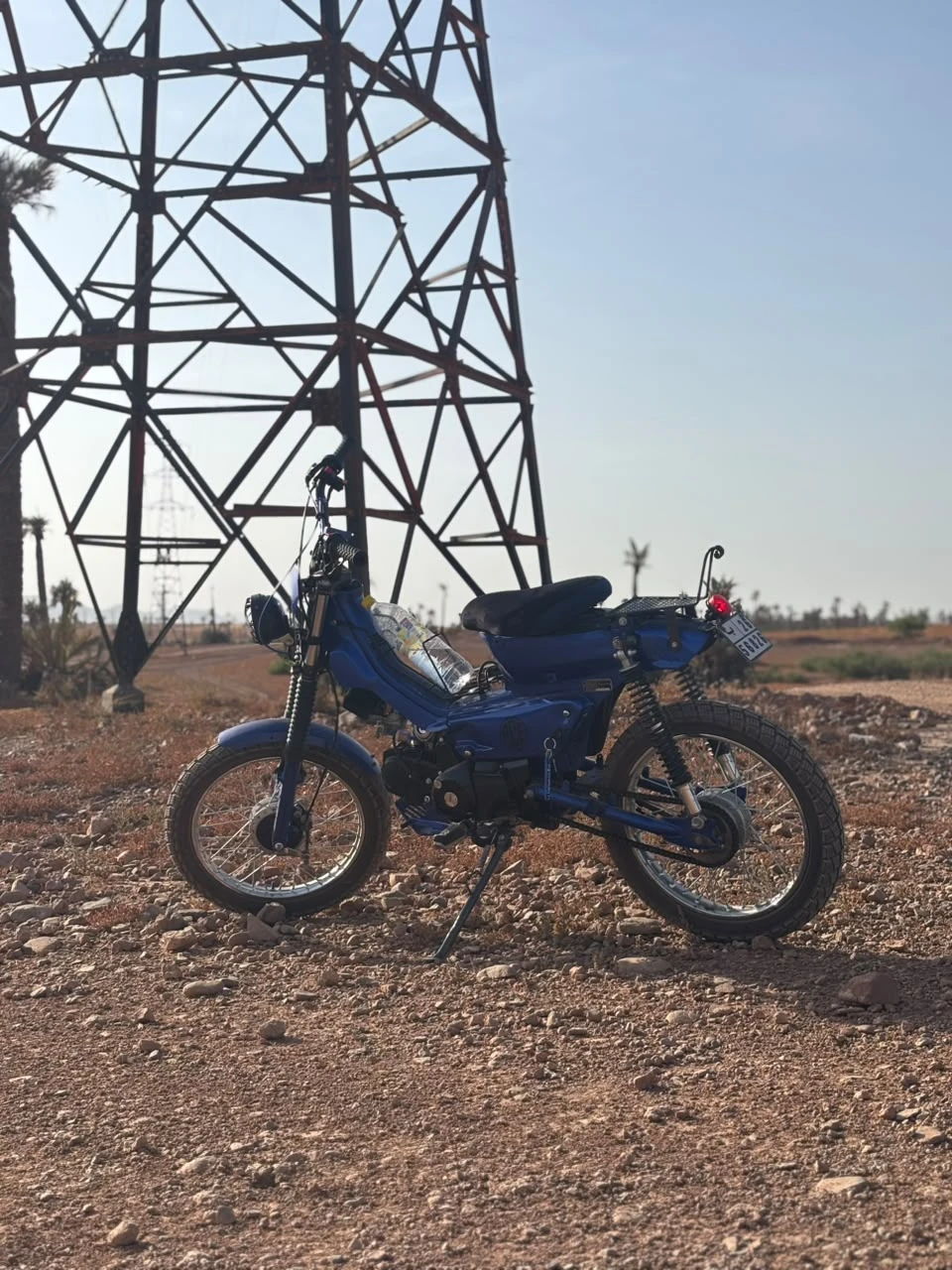 Sidi Bel Abbes custom blue motorcycle side profile on rocky ground near a transmission tower