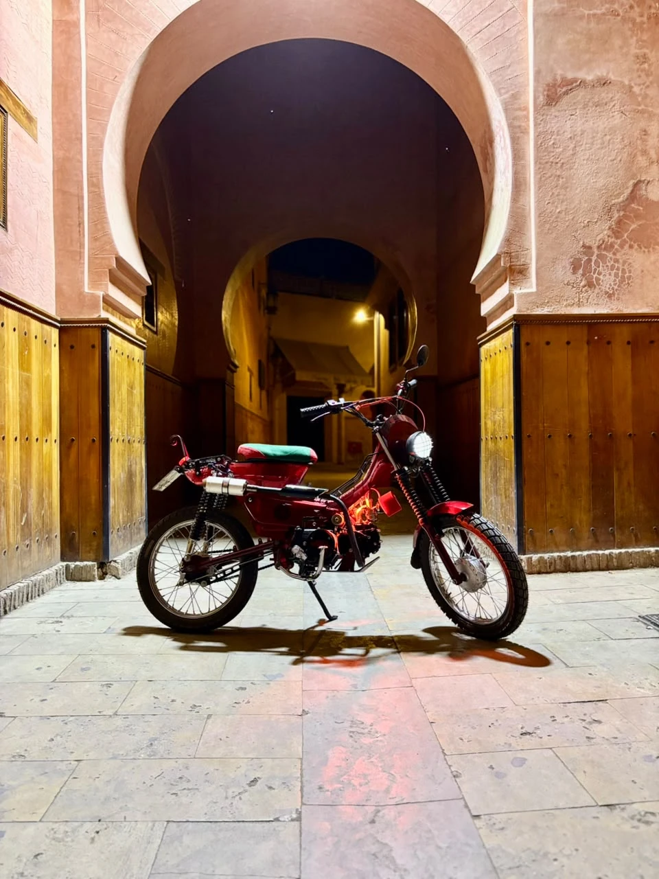 Sidi Youssef Ben Ali custom red motorcycle centered under a Marrakech archway