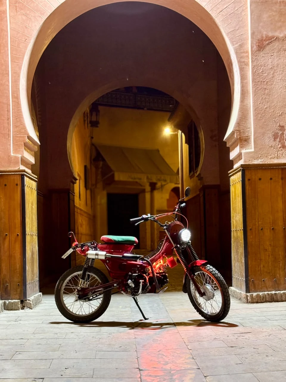 Sidi Youssef Ben Ali custom red motorcycle full view under a Marrakech archway at night