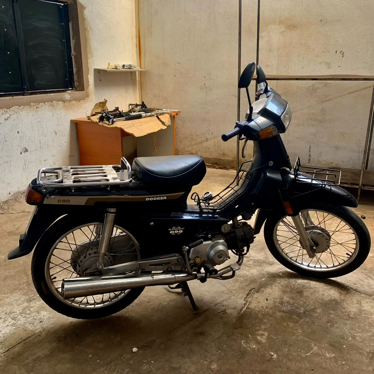Original black Honda Super Cub C90 donor motorcycle side profile inside the workshop