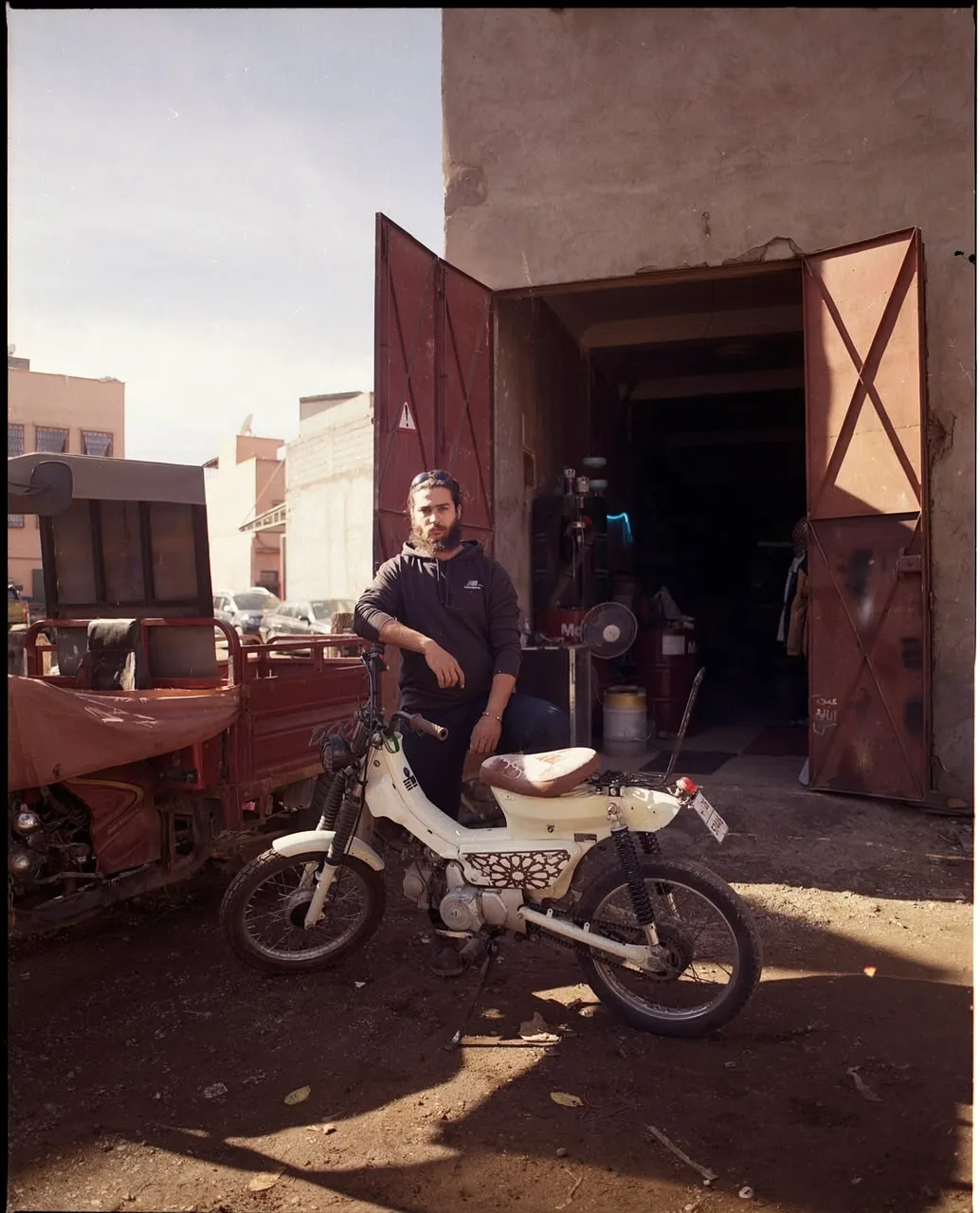 Mouad El Baraka standing beside a white custom motorcycle outside the BCE workshop