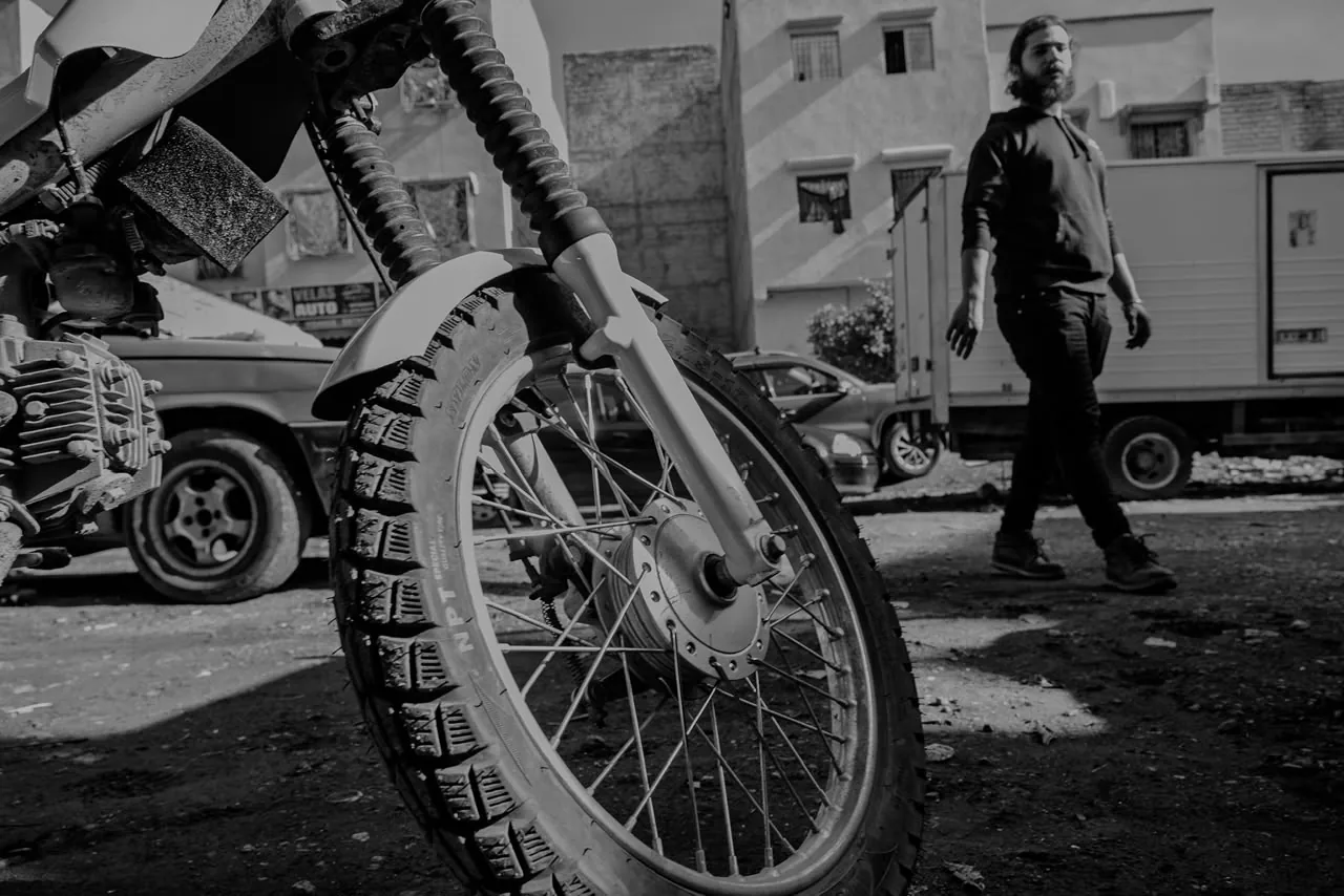 Low-angle black and white shot of a wheel with the creator walking in the background