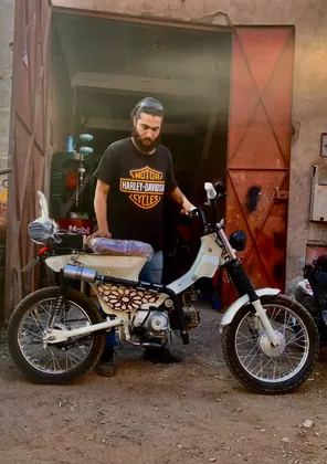 Mouad El Baraka standing with a completed white custom motorcycle at the workshop entrance thumbnail